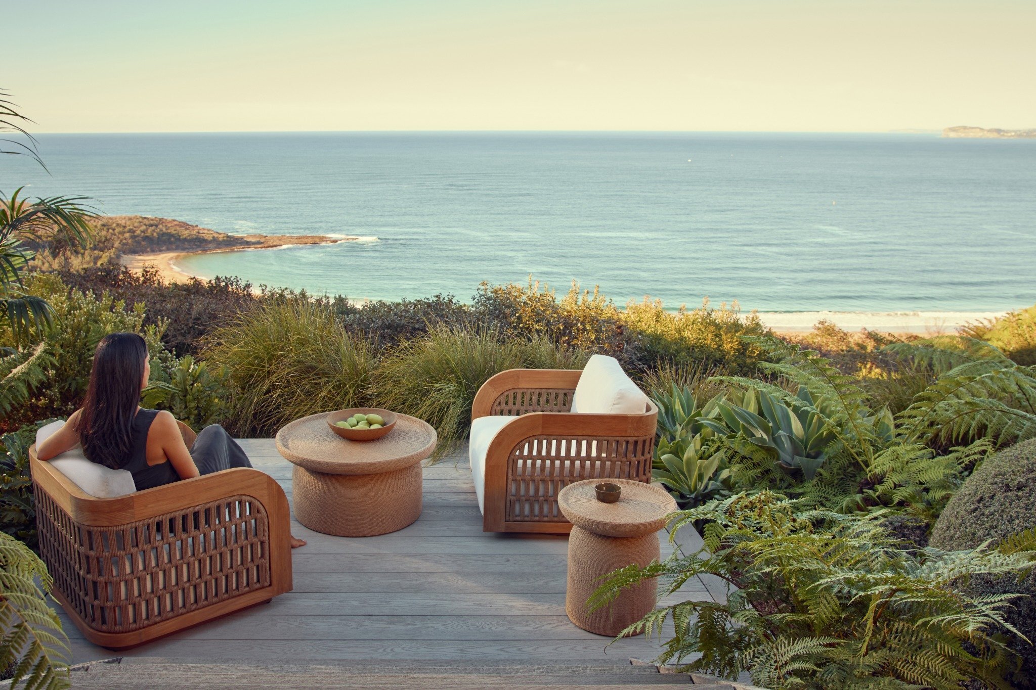 Outdoor chair in teak and woven detail, styled with woven coffee table in a landscaped garden.
