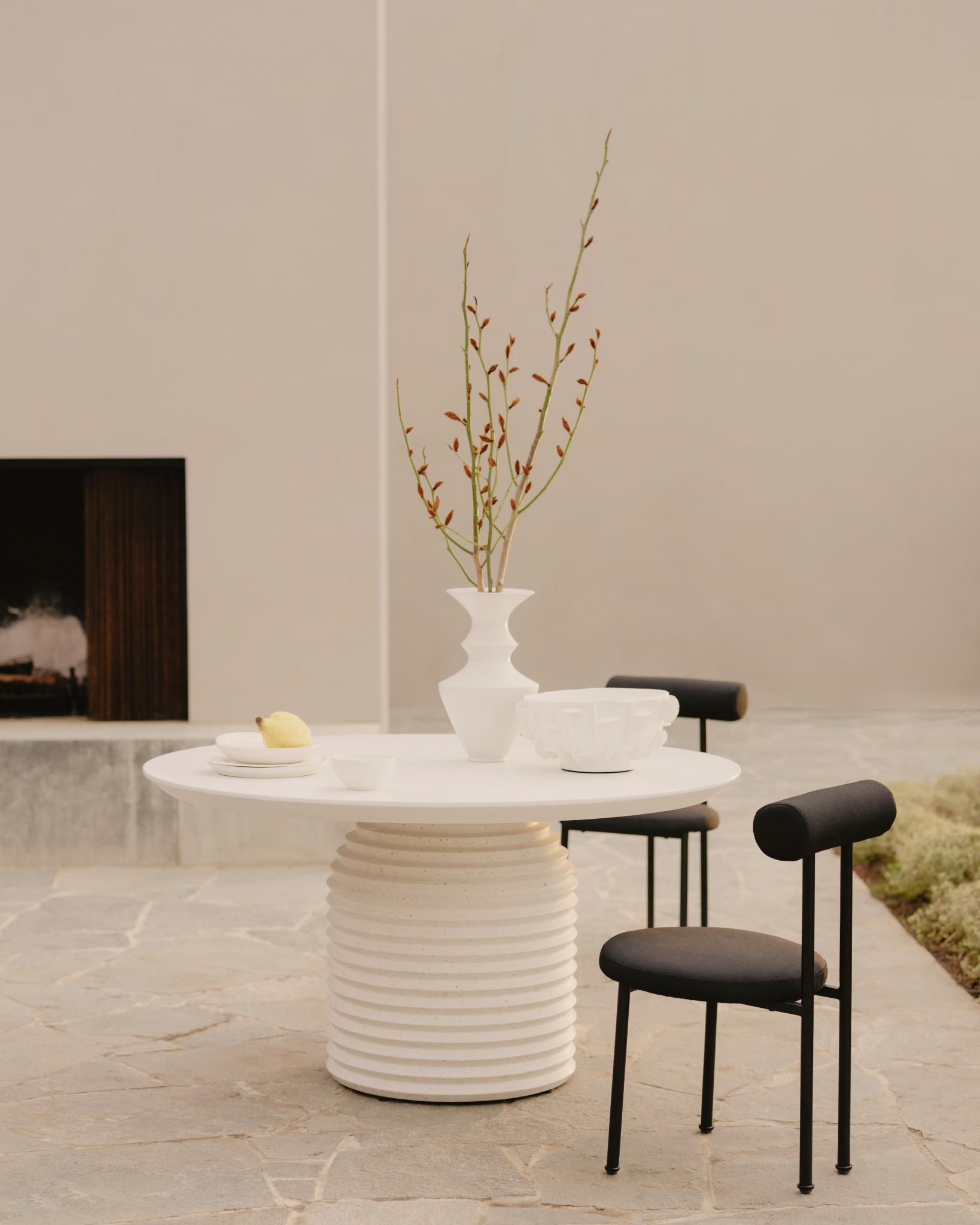 Outdoor dining table with sculptural base, paired with teak and rope dining chairs on a stone terrace.