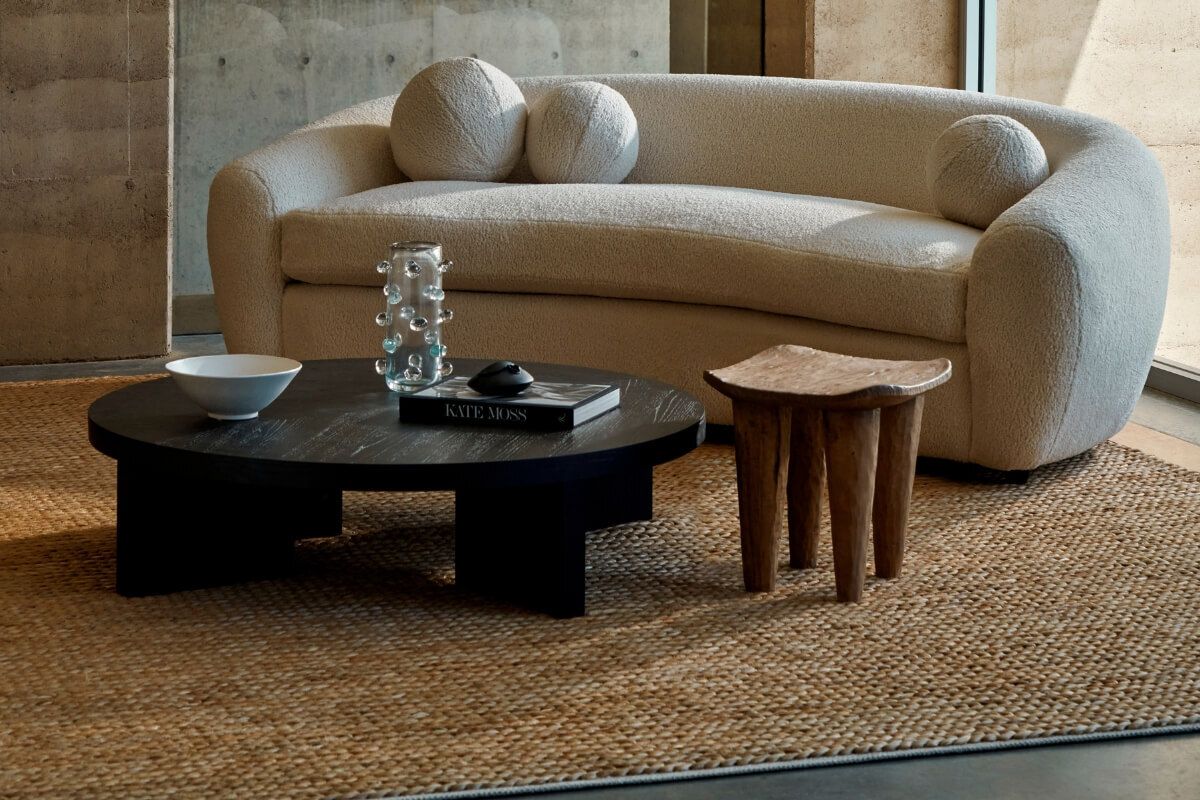 Black round coffee table styled with decorative objects, paired with a cream boucle curved sofa and woven jute rug in a modern living space.