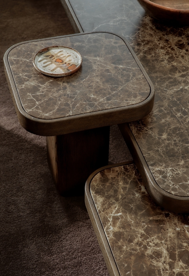 Close-up of brown marble nesting coffee tables with rounded square edges, featuring layered tabletops and a ceramic dish on the upper tier.