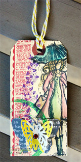 The umbrella girl on a mixed-media tag with a butterfly accent and script text.