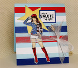 Red, white and blue striped card with a yellow star and a hand colored girl in a stars and stripes jacket saluting, beside a framed panel reading 'we SALUTE you'.