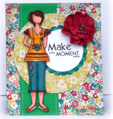 Floral print card with a green strip, a scalloped circle and a red paper flower, Suzie girl in an orange ruffled top and jeans with her camera, and 'Make every moment matter'.