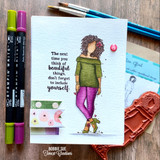 Watercolor card with Nia in an olive top and magenta pants, lettered 'The next time you think of beautiful things, don't forget to include yourself,' beside markers and the red rubber stamp.
