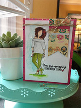 Card with Nia in a grey sweater and olive pants on floral paper, photographed beside a succulent.