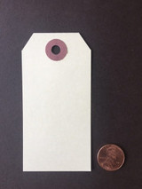Product photo of a blank manila shipping tag from Unity Stamp Co — a cream rectangular tag with a rounded top and reinforced hole, shown with a penny for scale.