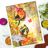 Vivid mixed media card in orange, yellow and magenta with heavy splatter, the poppies stamped in black over the layers and a small hello from all of us strip, styled with ink pads.