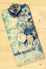 Blue watercolor tag with a stamped blossom, drippy ink, a lace heart topper and 'hello beautiful'