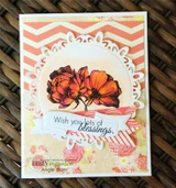 Card with the blooms colored in orange and red inside a white doily circle, layered over coral chevron and floral papers, 'Wish you lots of blessings' on a banner.