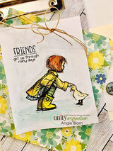 Kraft floral card with gold twine: the girl in a yellow raincoat leans toward her duckling under “FRIENDS get us through rainy days.”