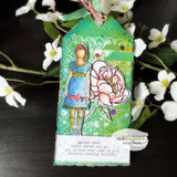 Girl in a blue and yellow dress with a pink peony on a green mixed-media tag, stamped 'Spread LOVE every where you go. Let no one ever come to you without leaving happier'.