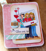 Pink card with a camera embellishment and a washi strip, three girlfriends stamped and colored holding a photo frame, red hearts above, and "girls just wanna have fun" on a banner.