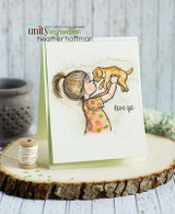 Clean card with the girl in a coral polka dot dress and a yellow puppy, 'love ya' stamped beside her, photographed on a wood slice with a spool of thread and green confetti.
