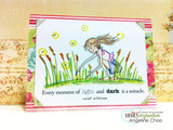 Card with the girl in a pink top and denim skirt bending into green grass and cattails, yellow-glowing fireflies around her, on floral paper, sentiment 'Every moment of light and dark is a miracle.'