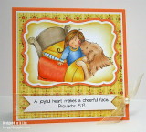 Card with the girl and her dog in an orange and yellow bed inside a white frame on patterned yellow paper, with an 'A joyful heart makes a cheerful face. Proverbs 15:13' banner