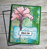 Mixed-media card with the flower in soft pink over green and blue painted layers with the word Smile on a white label.