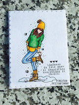 The girl in a green sweater with a mustard hat and tights on a postage-framed card over granite, with "Kindness is like snow, it beautifies everything it covers."