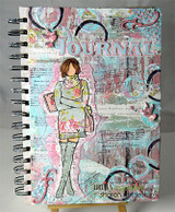 Mixed-media art journal page with Wakely Girl colored in soft pastels over collaged papers and the word 'Journal' lettered behind her.