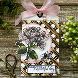 A tall kraft tag layered with a gold lattice panel, blossoms and a bee colored in soft pink and green, tied with pink ribbon.