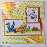 Green honeycomb card with the girl colored in a blue top and jeans lying on grass beside a brown bunny, stamped 'It's the Little Things.'