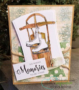 Kraft card layered over pine-branch paper; the wooden sled and pale ice skates rest on a die-cut panel above the 'So many memories' sentiment.