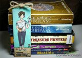 Card standing on a stack of hardback books, the girl coloured in a patterned tee and grey jeans on a teal and white panel with the good book sentiment underneath.