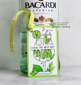 Green bordered gift tag with the lime filled mojito glass colored in greens and yellows, tied with yellow ribbon to a bottle of rum.