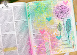 Flowers and feathers colored in the bright margins of an open Bible for journaling.