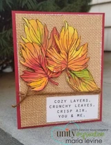 A burlap and red card with two big maple leaves colored in orange, yellow and green, above a stamped panel reading 'cozy layers, crunchy leaves, crisp air, you & me'.