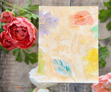 A soft cream card with leaves embossed in pastel rainbow inks and 'Fall' brush lettered faintly across the panel, styled with red and cream roses.