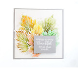 A grey card layered with maple leaves colored in a green to orange rainbow blend, with a small grey sentiment block in the center.