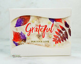 White card with a wavy die cut window revealing purple and red leaf prints on speckled paper, gold pearls scattered along the edge, Grateful in red script above for your love.