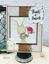 Card with a tan bunny in a pink bow tie holding red flowers over burlap, lace and newsprint layers with white paper flowers and the 'Thanks -a- Bunch' wreath