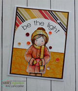 Card with the girl in a coral coat on a white panel with a gold leaf-print border, orange sequins, and be the light in an arc.