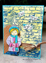 Card with the girl coloured in pink and blue against a bright blue and yellow stencilled brick wall, with be the light in cut letters and burlap ribbon.