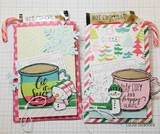 Two hot chocolate pocket cards in pink and green prints, each with a coloured mug, one stamped 'stay cozy and happy always'.