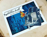 Card with the barn wall inked blue behind a vintage camera: 'Possibilities await. Capture your story.'