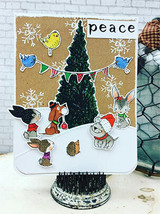 A dimensional woodland scene of a tall tree, a bird banner and animals in the snow on a kraft-and-brick background, with "Peace."