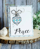 A blue plaid card with the ornament stamped in outline and colored pale blue, tied with silver twine and a small bell.
