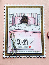 Pink card with the girl colored under a cozy quilt and a 'SORRY you had a bad day' note tied with twine.
