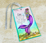 Slimline tag with the mermaid colored in purple and turquoise over a blended aqua and green sky with floral shells.
