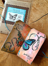 Mixed-media tag set on wood with teal thread: the butterfly colored in rainbow inks with hand-drawn swirls and the “let today be the start of something new” sentiment.