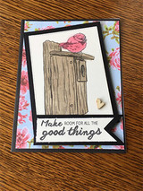 A black and floral card with the little bird colored coral perched on its wooden birdhouse, above a black banner reading 'Make room for all the good things'.
