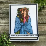 A black framed card with two friends wrapped in one blue blanket, flower crowns in their hair, colored in soft pinks and blues, above a black strip reading 'the best of friends are wrapped in love'.