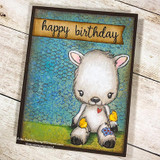 Card with the lamb coloured cream and grey with a red heart and patched paw, sitting on green grass over a teal honeycomb background, with a "happy birthday" banner above.