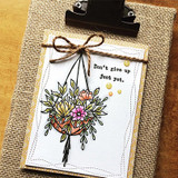The hanging planter colored with pink and yellow blooms on a white card with a twine bow, captioned "Do not give up just yet."