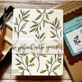 Scattered leaf sprigs stamped over a cream card with 'be patient with yourself.'