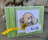 Green wood-print card with the bunny in soft greys and a yellow daisy, a yellow ribbon, and a panel reading Some days require extra hugs.