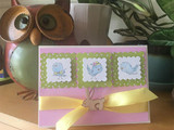 Trio of small framed bird panels on a pale purple card with a yellow ribbon.