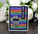Grinning cake on a rainbow-striped panel, 'Happy Birthday.'